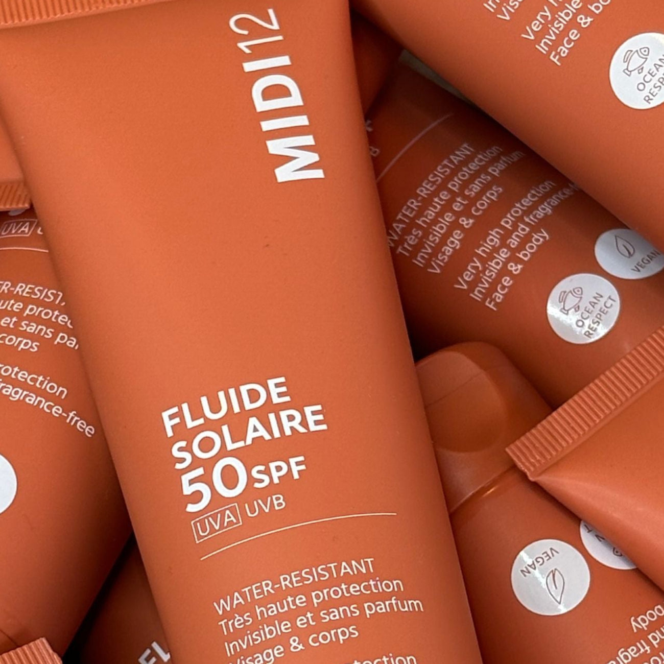 Multiple bottles of Fluide Solaire SPF 50 by MID12 on a white background